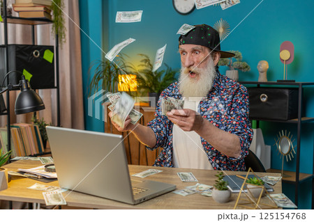 Money cash dollar falling on senior man with laptop celebrating success winning goal achievement 125154768