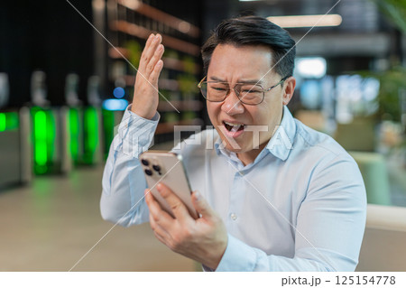 Upset businessman using smartphone becomes shocked sudden lottery results in modern office lobby 125154778