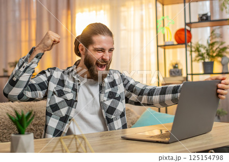 Young man man opens laptop at home wow great winning result in an online course celebrates victory Young man man opens laptop at home wow great winning result in an online course celebrates victory 125154798