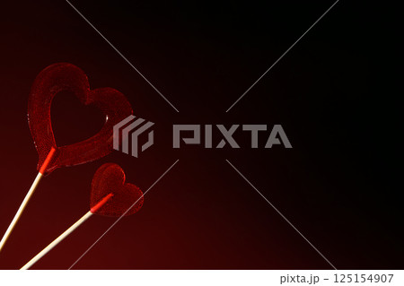 Love. Two red transparent heart-shaped lollipops on a dark red background. Horizontal banner for Valentine's Day.  125154907