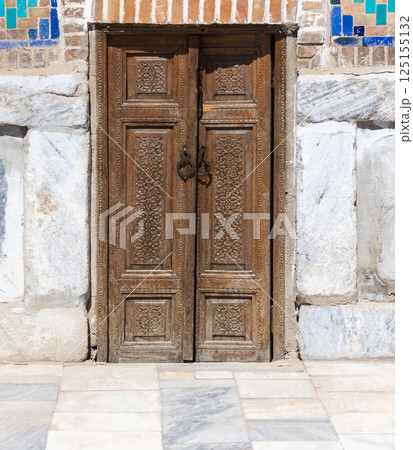 Intricately designed wooden doors set within a stone and brick wall 125155132