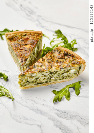 Delicious spinach and feta quiche slices with fresh arugula on marble 125155148