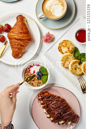 Woman having delicious breakfast with croissants, granola, pancakes and coffee Woman having delicious breakfast with croissants, granola, pancakes and coffee 125155159