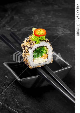 Chopsticks holding uramaki sushi roll with sesame seeds and vegetables over soy sauce Chopsticks holding uramaki sushi roll with sesame seeds and vegetables over soy sauce 125155167