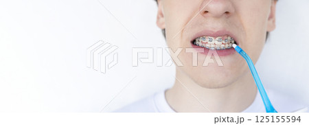 A young unrecognizable man with braces cleaning his teeth with oral irrigator. A young unrecognizable man with braces cleaning his teeth with oral irrigator. 125155594