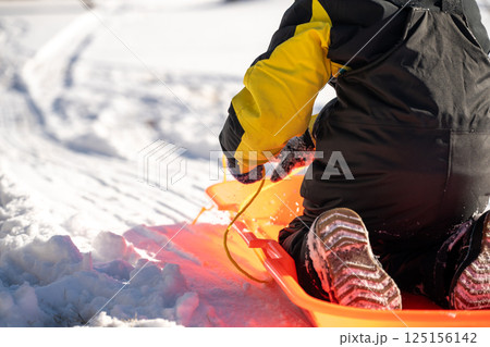 Selective focus on the snow boot of a child going down a hill on a sled Selective focus on the snow boot of a child going down a hill on a sled 125156142