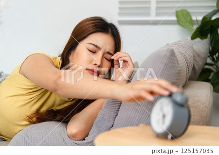 Morning Routine and Waking Up. A woman groggily reaching for an alarm clock to turn it off and start her day. 125157035