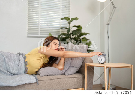 Waking Up from Sleep. A young woman reaching for her alarm clock in a gentle morning light, transitioning from sleep to waking state. 125157054