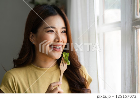 Healthy Eating and Daily Inspiration. A woman smiling with her salad while gazing through a window. 125157072