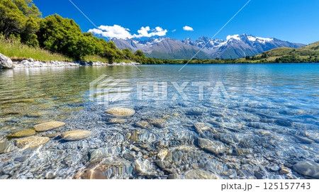 Crystal clear lake with rocky shoreline and snow-capped mountain range under blue sky. Crystal clear lake with rocky shoreline and snow-capped mountain range under blue sky. 125157743