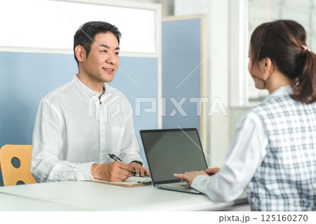 窓口で受付をする男性顧客と窓口対応する事務員の女性スタッフ 125160270