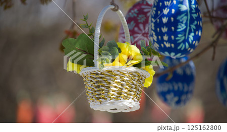 A small flower basket filled with yellow pansies hangs with decorated easter eggs. A small flower basket filled with yellow pansies hangs with decorated easter eggs. 125162800