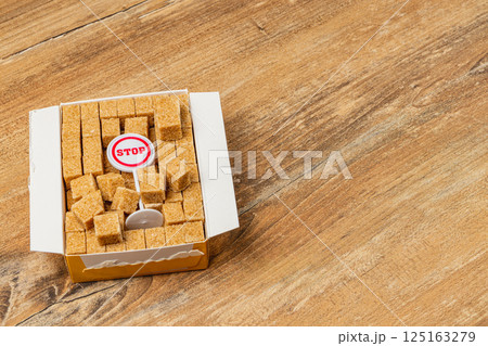 Brown sugar cubes in a box with a stop sign on a wooden surface Brown sugar cubes in a box with a stop sign on a wooden surface 125163279