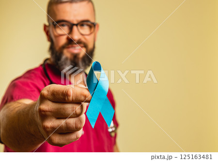 Medical professional highlights awareness with blue ribbon in clinic setting Medical professional highlights awareness with blue ribbon in clinic setting 125163481