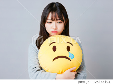 絵文字のクッションを持って悲しんでいる若い女性 125165193