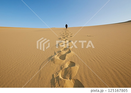 Tourist with a stick walking through the desert in the landscape, path footprints in the sand Tourist with a stick walking through the desert in the landscape, path footprints in the sand 125167805