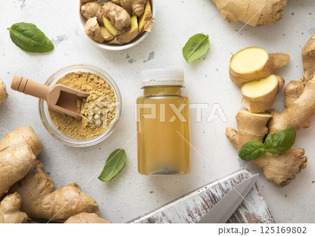 Bottle of immune ginger energy shot drink with ginger root and grounded powder on light background. Bottle of immune ginger energy shot drink with ginger root and grounded powder on light background. 125169802