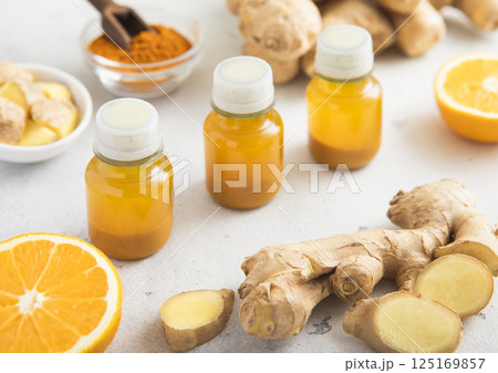 Turmeric energy shot immune drink with ginger root and ripe oranges on light background.Macro. Turmeric energy shot immune drink with ginger root and ripe oranges on light background.Macro. 125169857
