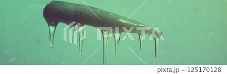 An icicle dangles with a sharp point and dripping tip against a grunge background. An icicle dangles with a sharp point and dripping tip against a grunge background. 125170128
