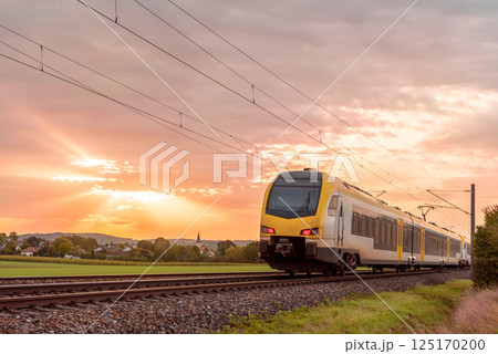 Passenger train traveling at sunrise near a german village Passenger train traveling at sunrise near a german village 125170200