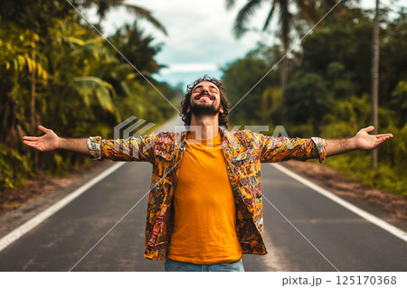 A joyful summer scene featuring a man with his hands raised, basking in the warmth of the sun. The image captures a carefree and happy moment, possibly with palms in the background 125170368