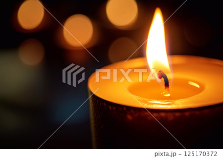 Single candle burning at night with soft flame and warm glow. Serene and peaceful atmosphere, symbolizing light, warmth, and memorial reflection 125170372