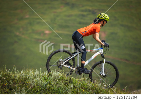 Woman riding mountain bike on beautiful flowering grassland mountain top Woman riding mountain bike on beautiful flowering grassland mountain top 125171204