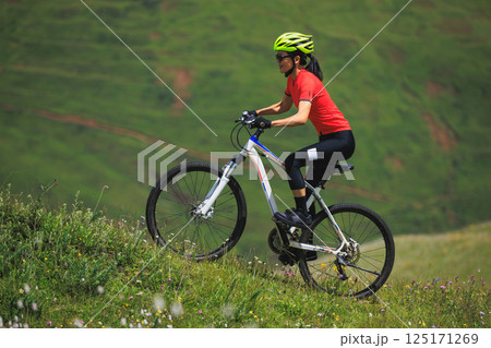 Fitness aisan woman riding mountain bike on beautiful flowering grassland mountain top Fitness aisan woman riding mountain bike on beautiful flowering grassland mountain top 125171269