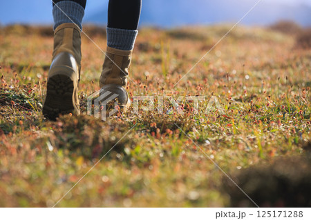 Hiker legs wearing leather boots hiking on high altitude mountain top Hiker legs wearing leather boots hiking on high altitude mountain top 125171288