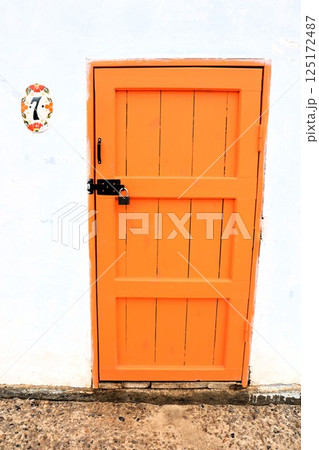 A Vibrant Orange Door Set Against a White Wall, Showcasing Beauty and Artistic Charm A Vibrant Orange Door Set Against a White Wall, Showcasing Beauty and Artistic Charm 125172487
