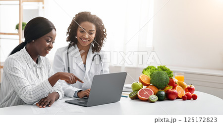 African women dietician and patient looking at laptop screen at dietologist cabinet, copy space 125172823