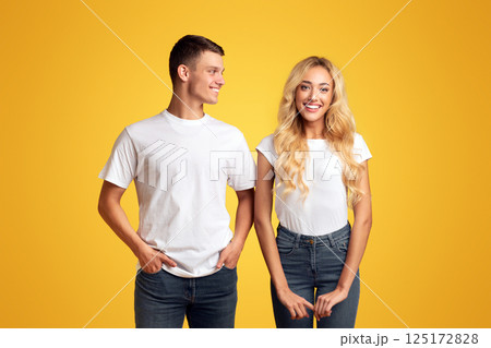 Happy beautiful girl and handsome young guy posing to camera over yellow background, free space 125172828