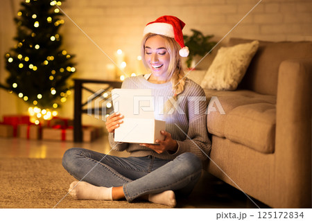 Christmas time. Happy girl with santa hat opening gift box over xmas tree 125172834