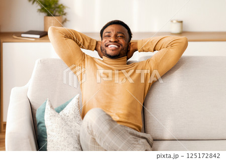 Relaxed African American Man Resting Sitting On Couch Holding Hands Behind Head At Home. Enjoying Weekend. Free Space 125172842