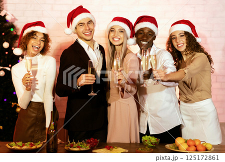 Merry Christmas Concept. Joyful Young People Holding Champagne Glasses Smiling At Camera Standing Next To Table At Home 125172861