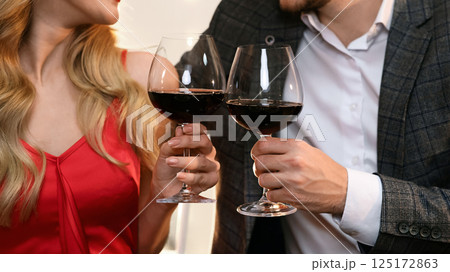 Cheers. Closeup of glasses with red wine in hands of happy couple on date in restaurant, romantic pair celebrating Valentine's day together, crop Cheers. Closeup of glasses with red wine in hands of happy couple on date in restaurant, romantic pair celebrating Valentine's day together, crop 125172863