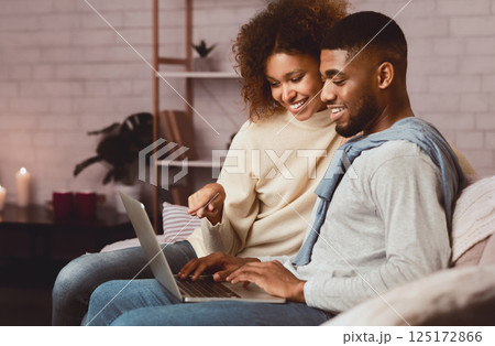 Happy afro spouses using laptop, spending weekend at home and searching film Happy afro spouses using laptop, spending weekend at home and searching film 125172866
