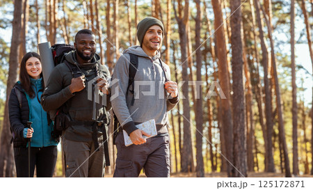 Three cheerful multiracial friends hiking by forest, going towards free space, side view Three cheerful multiracial friends hiking by forest, going towards free space, side view 125172871