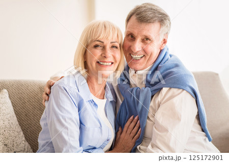 Happy mature couple embracing and smiling to camera, sitting on sofa at home 125172901