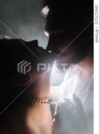 Silhouette of a young couple in the dark and smoke. A guy and a girl in the smoke in a dark room kiss, hug and show passion Silhouette of a young couple in the dark and smoke. A guy and a girl in the smoke in a dark room kiss, hug and show passion 125172943