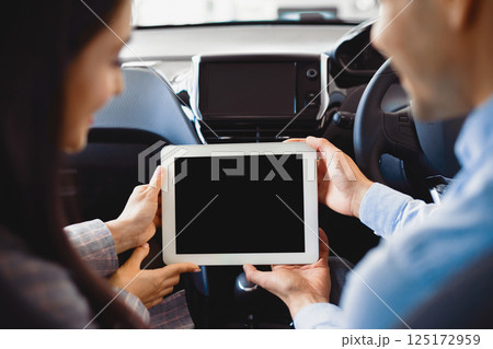Couple Using Digital Tablet With Empty Screen Sitting In New Car In Dealership Center. Mockup, Back View, Selective Focus Couple Using Digital Tablet With Empty Screen Sitting In New Car In Dealership Center. Mockup, Back View, Selective Focus 125172959