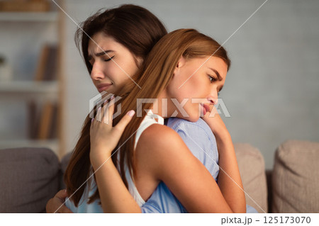 Compassionate Girl Hugging Crying Friend Supporting Her After Breakup With Boyfriend Sitting On Sofa Indoor. Selective Focus Compassionate Girl Hugging Crying Friend Supporting Her After Breakup With Boyfriend Sitting On Sofa Indoor. Selective Focus 125173070