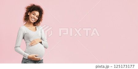True mother love. African-american pregnant woman hugging her belly and smiling to camera, pink background with free space 125173177