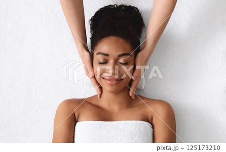 Top view of relaxed black young woman having facial massage over white background 125173210