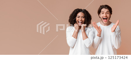Interracial couple emotionally rejoicing success, raising hands and exclaiming with excitement over yellow studio background Interracial couple emotionally rejoicing success, raising hands and exclaiming with excitement over yellow studio background 125173424