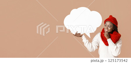 Pretty interested woman in winter hat holding communication bubble, touching her chin, beige studio background 125173542