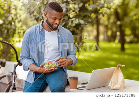 Lunch Outdoors. Smiling Black Guy Eating Vegetable Salad And Drinking Coffee While Relaxing With Laptop In Park During Break At Work Lunch Outdoors. Smiling Black Guy Eating Vegetable Salad And Drinking Coffee While Relaxing With Laptop In Park During Break At Work 125173599