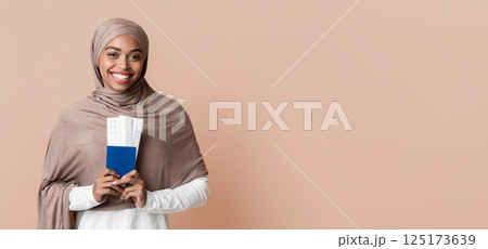 Ready for travel. Happy afro muslim woman in hijab holding passport and tickets, going to vacation, yellow background with empty space 125173639