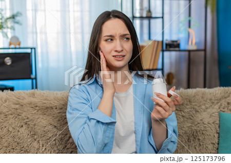 Young woman suffering toothache holding cheek in pain tiredly searching and taking painkiller pills 125173796