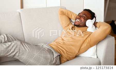 Relax. Happy Afro Man In Wireless Headphones Listening To Music Lying On Sofa At Home Relax. Happy Afro Man In Wireless Headphones Listening To Music Lying On Sofa At Home 125173814
